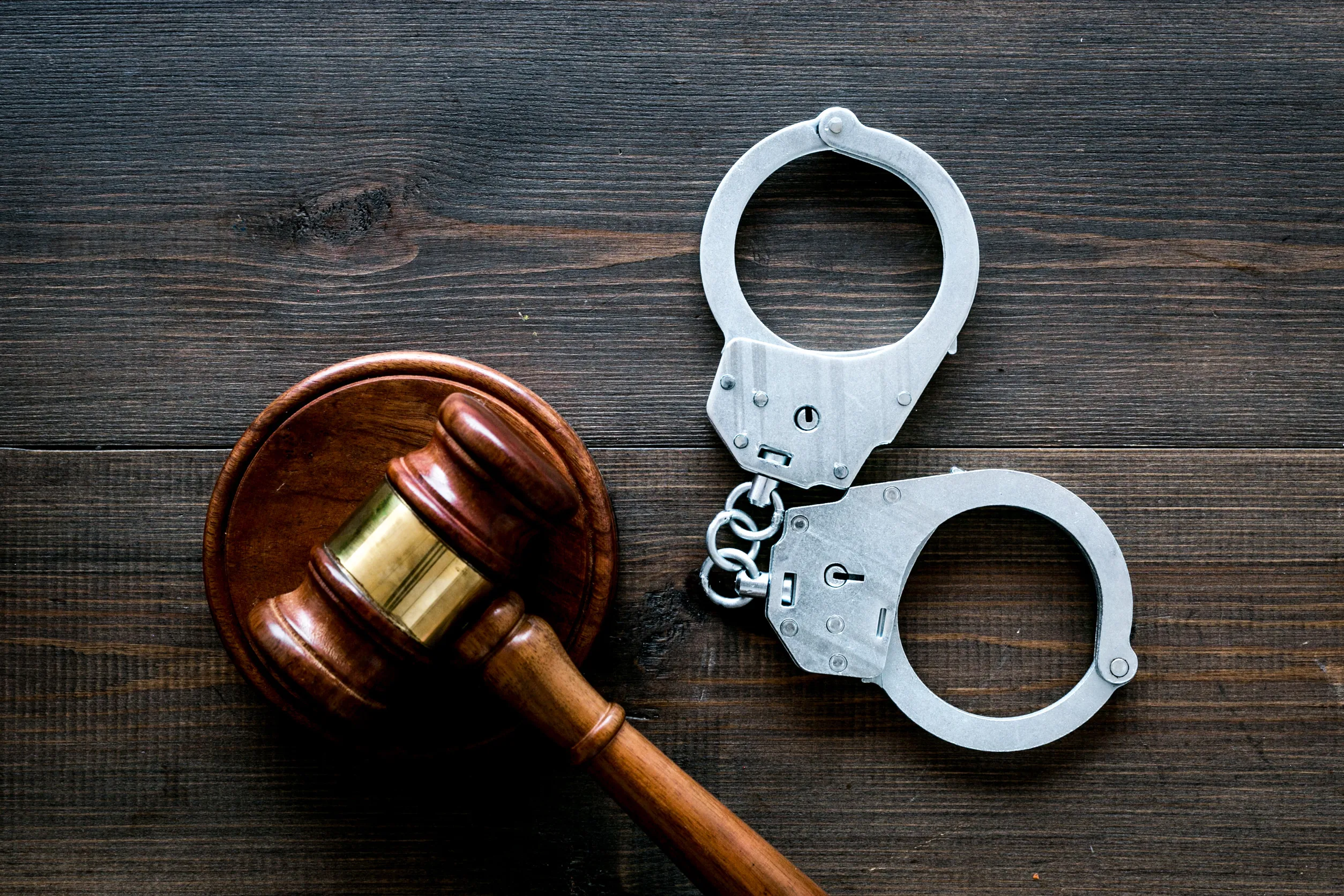 Metal handcuffs near judge gavel on dark wooden background top view