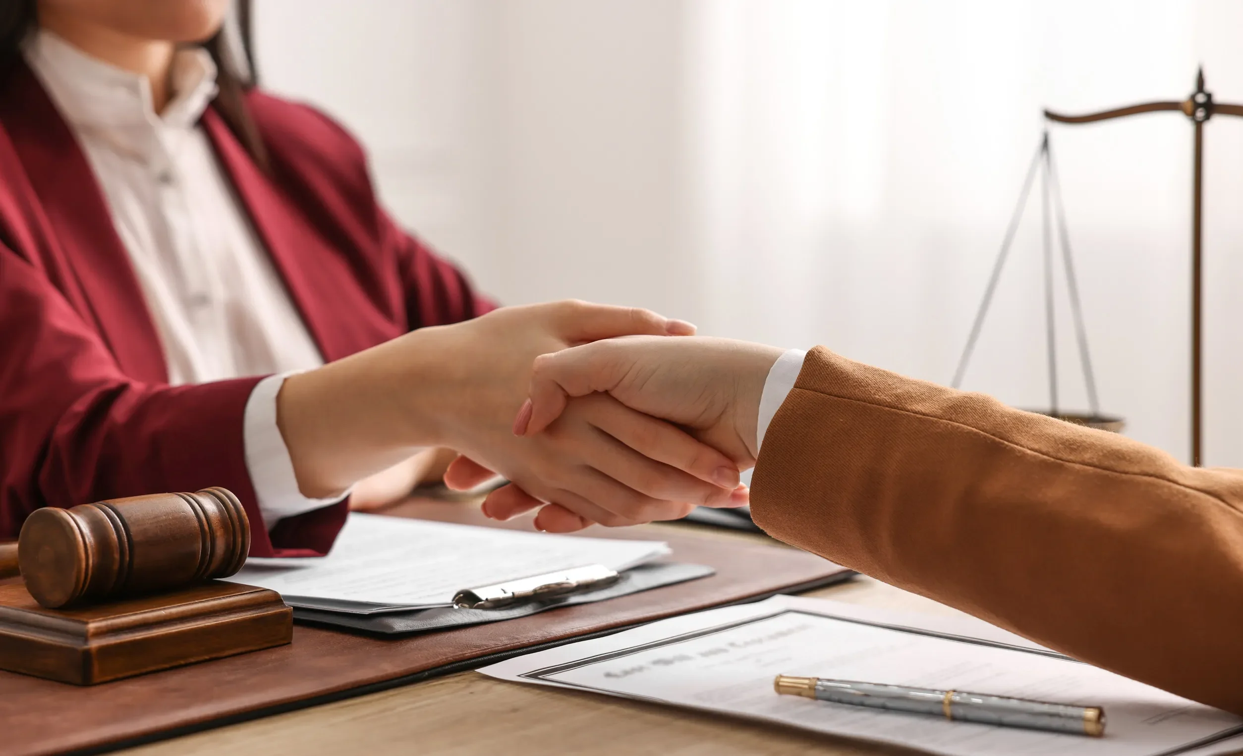 Notary shaking hands with client at wooden table in office, closeup